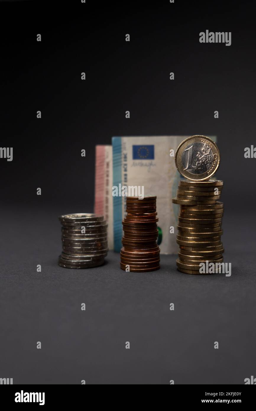 Una moneta in euro su sfondo scuro. Concetto di monete in euro impilate con banconote in euro dietro e fuori fuoco. Spazio di copia. Foto Stock