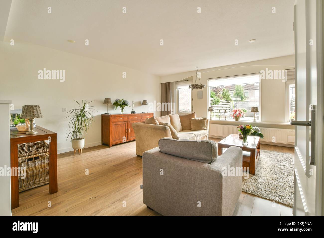 Divano ad angolo con morbidi cuscini situato sotto un elegante lampadario vicino alla TV nel luminoso soggiorno vicino alla cucina Foto Stock