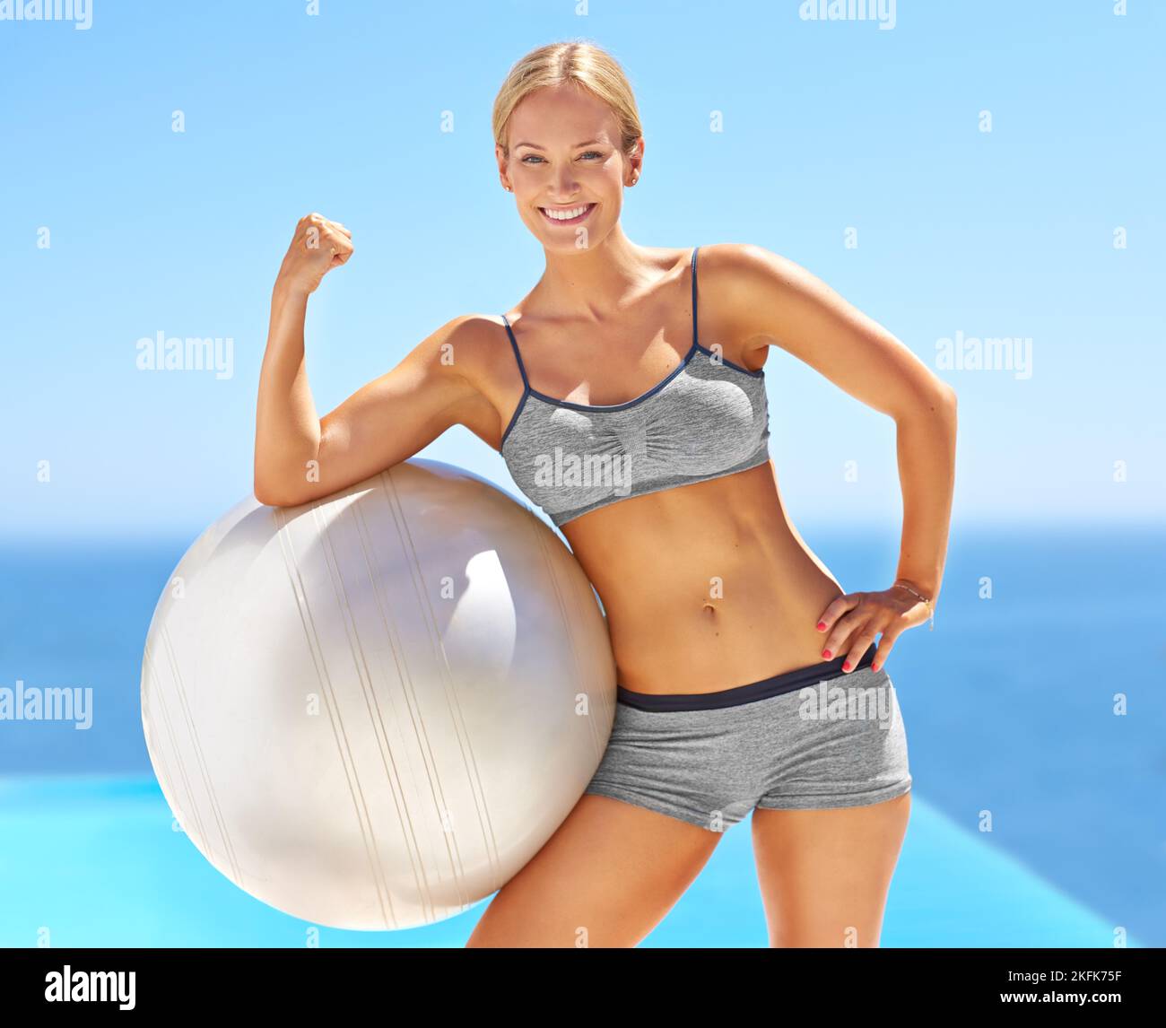 Sentirsi più forti ogni giorno. Ritratto di una giovane donna attraente flexing il suo bicep su una sfera di esercitazione. Foto Stock