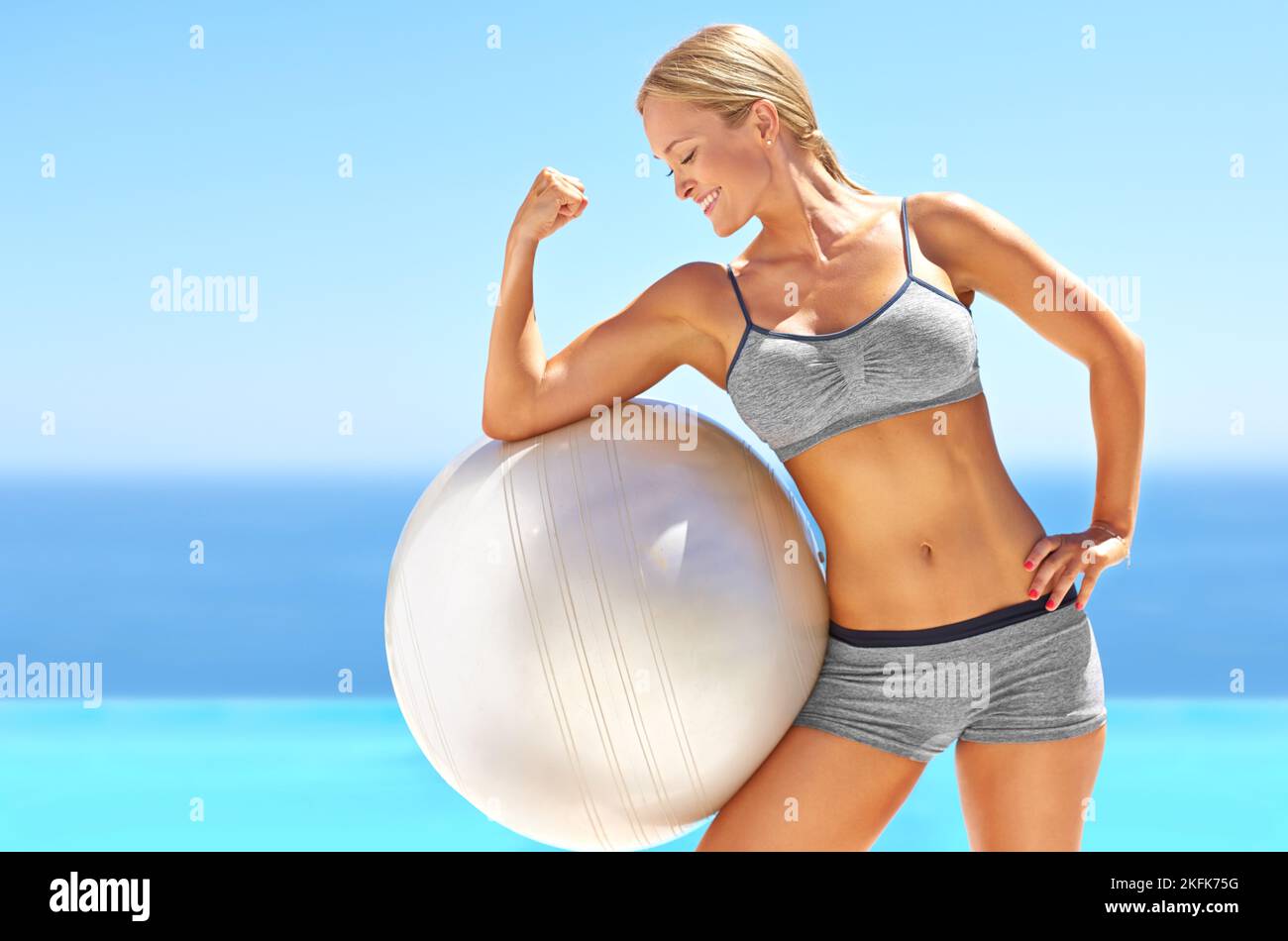 Possedere il suo workout. Una giovane donna attraente che flette il suo bicep su una sfera di esercitazione. Foto Stock