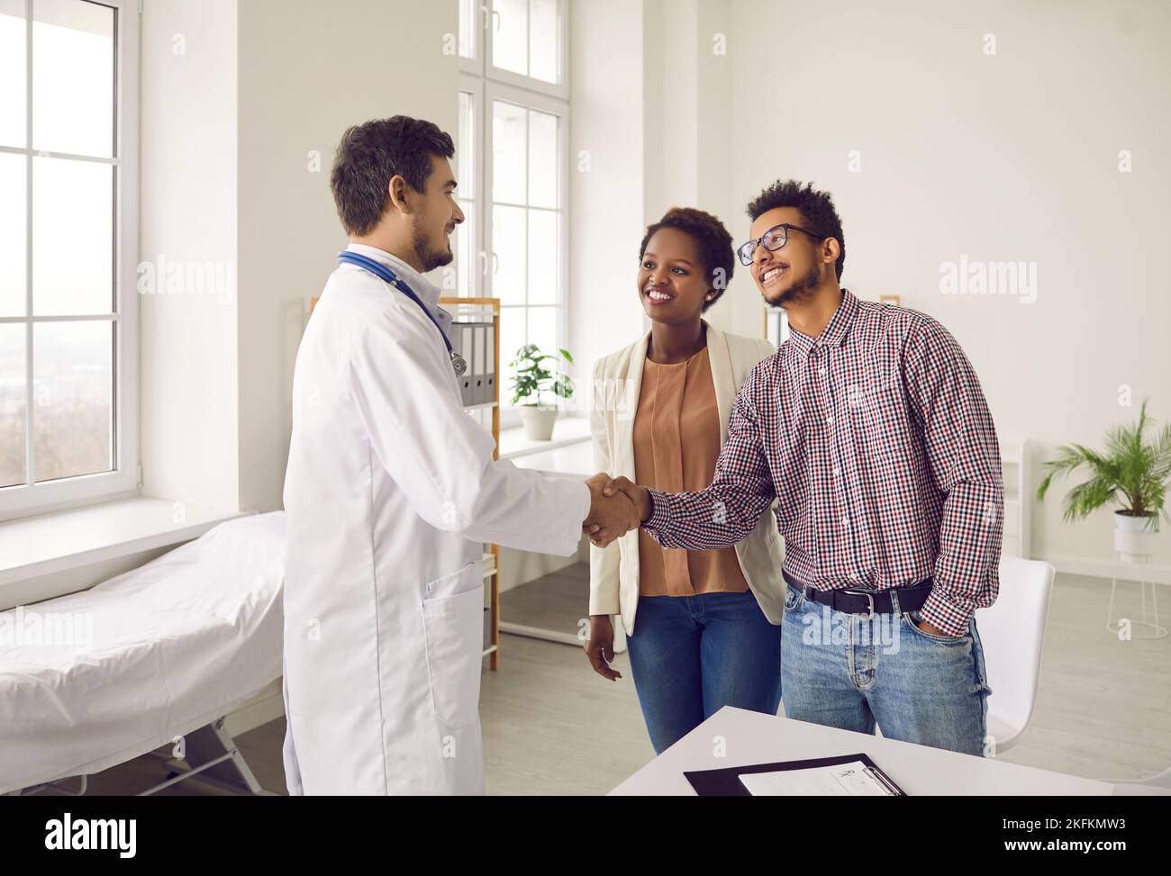 Giovane coppia scuote le mani con un medico professionista che si occupa della pianificazione della gravidanza. Foto Stock