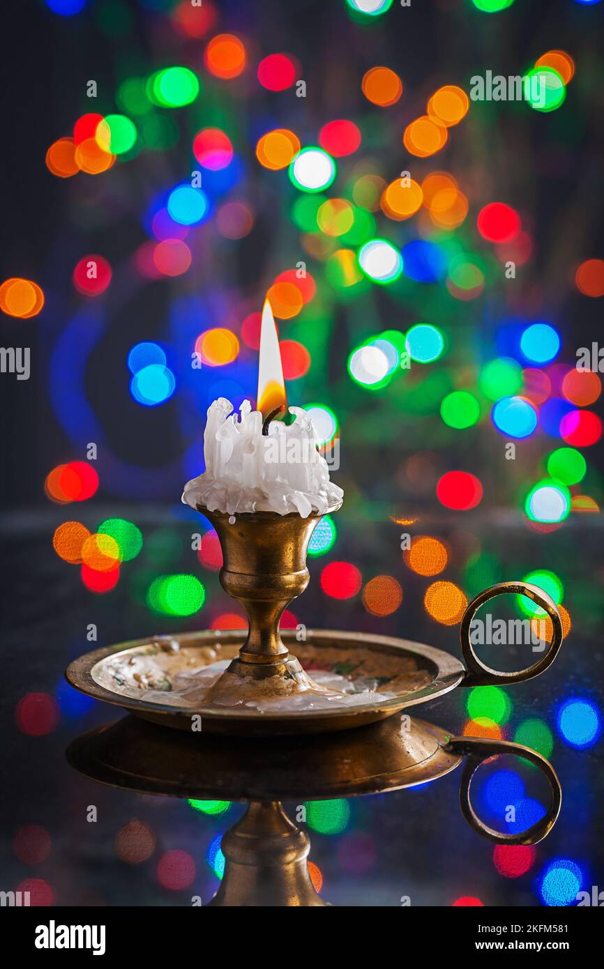 candela vecchia incandescente in candelabro d'pouazione sulla superficie dello specchio con bokeh multicolore Foto Stock