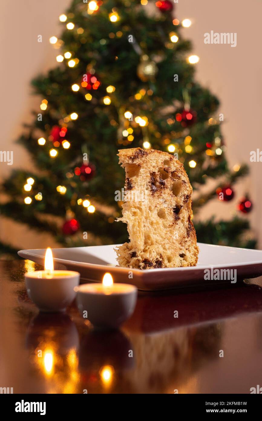 Goiânia, Goias, Brasile – 18 novembre 2022: Una fetta di panettone all'interno del piatto, due candele accese e le luci dell'albero di Natale. Foto Stock