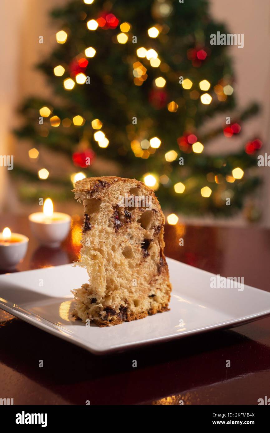 Goiânia, Goias, Brasile – 18 novembre 2022: Una fetta di panettone all'interno del piatto, due candele accese e le luci dell'albero di Natale. Foto Stock