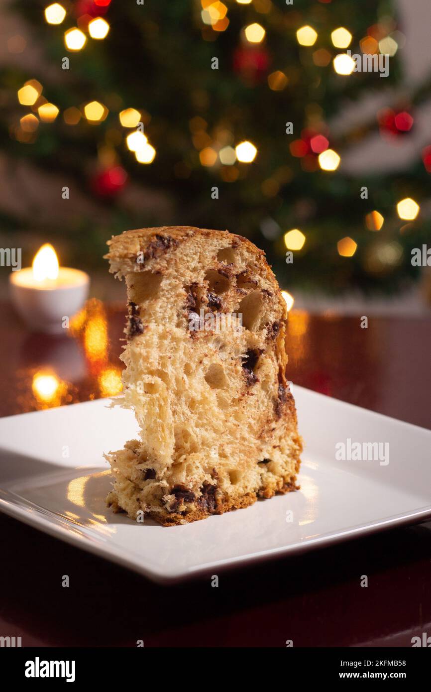 Goiânia, Goias, Brasile – 18 novembre 2022: Una fetta di panettone all'interno del piatto, due candele accese e le luci dell'albero di Natale. Foto Stock