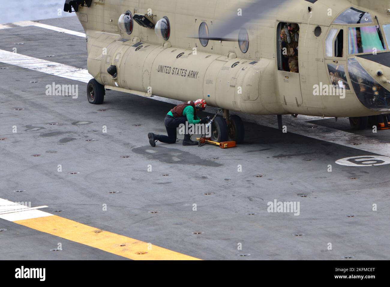 Un marinaio assegnato alla USS Ronald Reagan (CVN 76) posiziona blocchi di zeppa sotto il carrello di atterraggio di un elicottero CH-47F Chinook dell'esercito statunitense. Soldiers from B Company, 3-2 General Support Aviation Battalion, 2nd Combat Aviation Brigade condusse atterraggi con elicotteri CH-47F Chinook sull'unico portaerei della Marina statunitense, USS Ronald Reagan (CVN 76), nelle acque ad est della penisola coreana il 26 settembre 2022. Le qualifiche di atterraggio sul ponte sono condotte per certificare i membri dell'equipaggio e i piloti che atterrano su una nave. Questa formazione è stata condotta in parte con il Mari Foto Stock