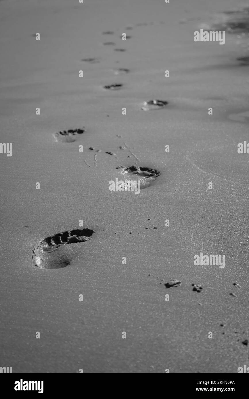 Passi in sabbia, bianco e nero. Impronte in spiaggia, monocromatiche. Concetto di passeggiata. Passi umani sulla riva del mare. Passeggiata a piedi nudi sulla costa. Foto Stock