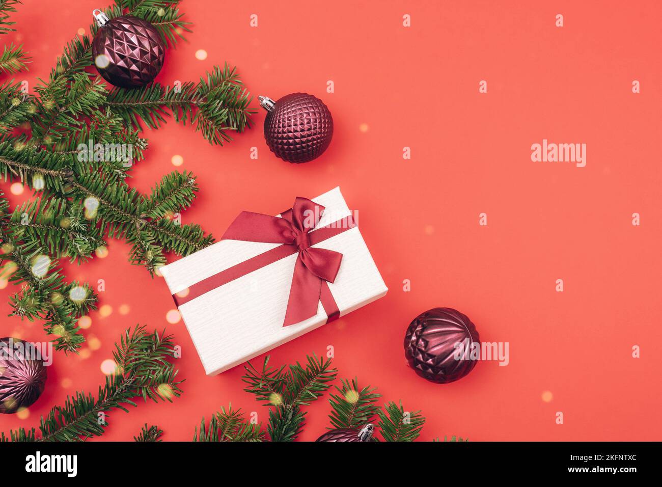 Scatola regalo e rami di abete con decorazioni natalizie e luci bokeh su sfondo rosso. Concetto di vacanza invernale. Vista dall'alto, disposizione piatta, spazio di copia. Foto Stock