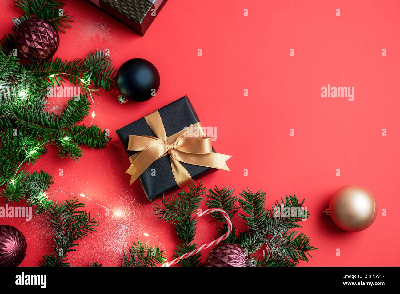 Scatole regalo, palline di Natale colorate e rami di abete con decorazioni natalizie e luci bokeh su sfondo rosso. Concetto di vacanza invernale. Vista dall'alto Foto Stock