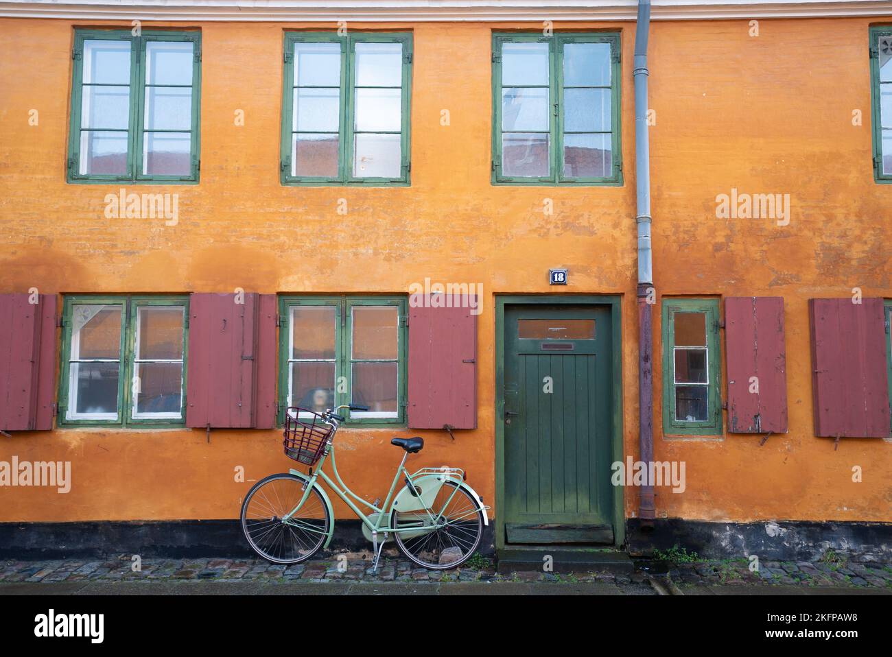 Biciclette fuori da una casa a Nyboder, uno storico quartiere di case di fila di ex caserme navali a Copenaghen, Danimarca. Case gialle a Copenhagen. Foto Stock