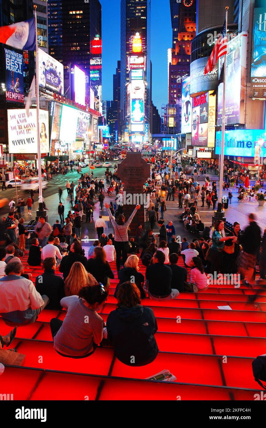 Una folla si riunisce sulle scale e sui sedili dell'edificio TKTS per avere una vista delle schede video illuminate con pubblicità a Times Square, New York Foto Stock