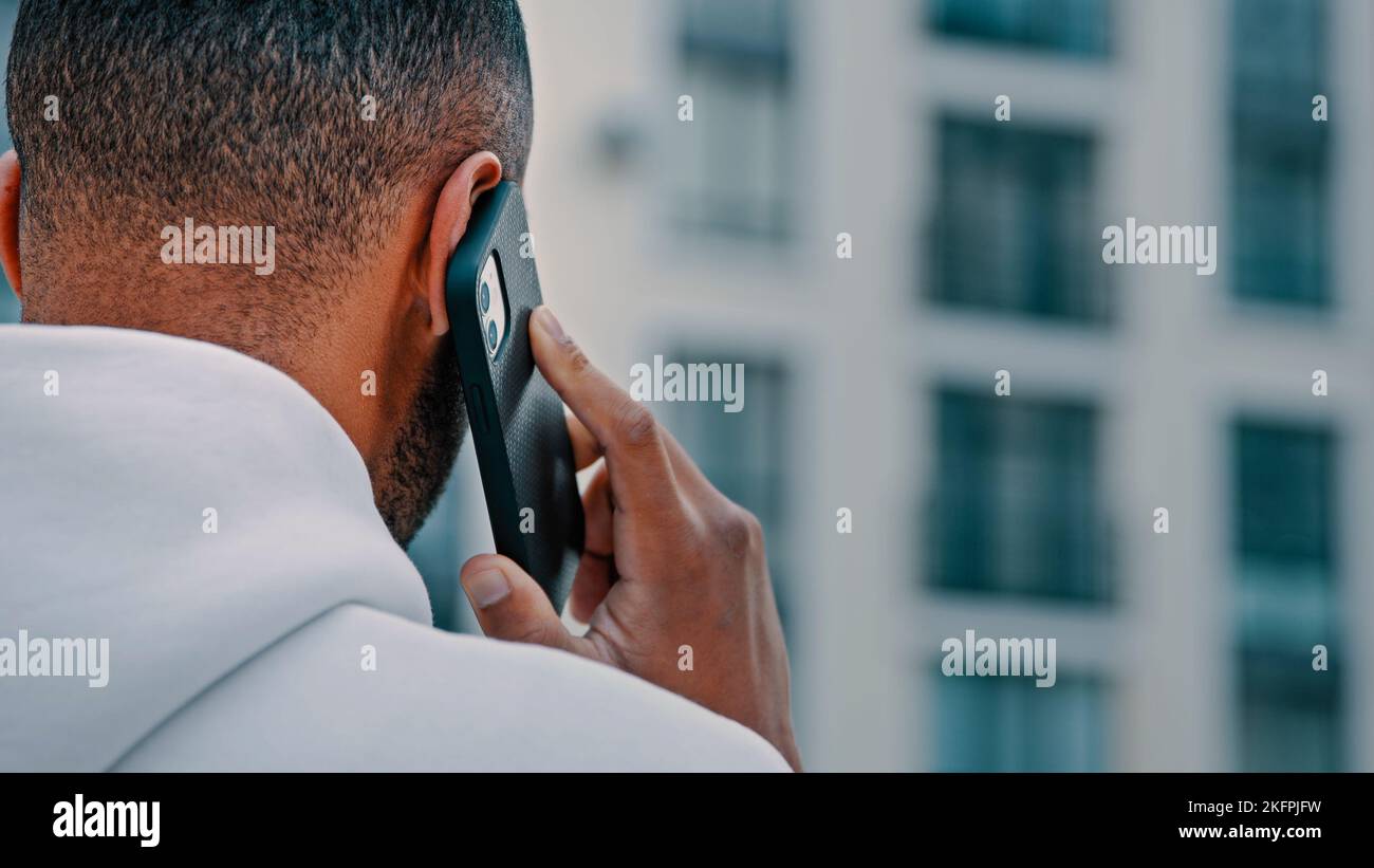 Vista posteriore uomo africano adulto latina freelancer parlare cellulare esterno città strada parlare telefono cellulare conversazione a distanza uso gratuito wi-fi al di fuori moderno Foto Stock