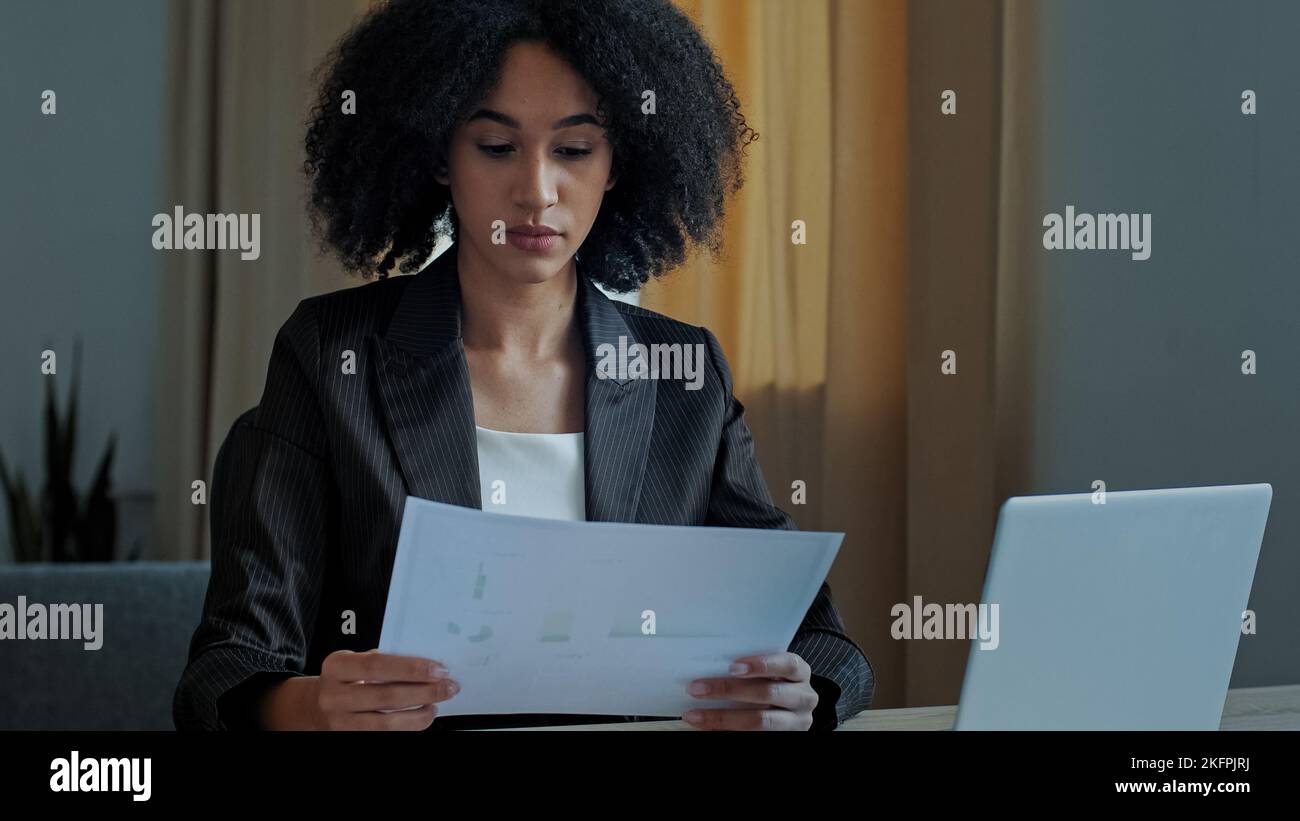 Insegnante africano lavoratore business donna lavorare con documenti grafici a casa ufficio controllo documentazione inserire dati finanziari al computer portatile elaborazione on-line Foto Stock
