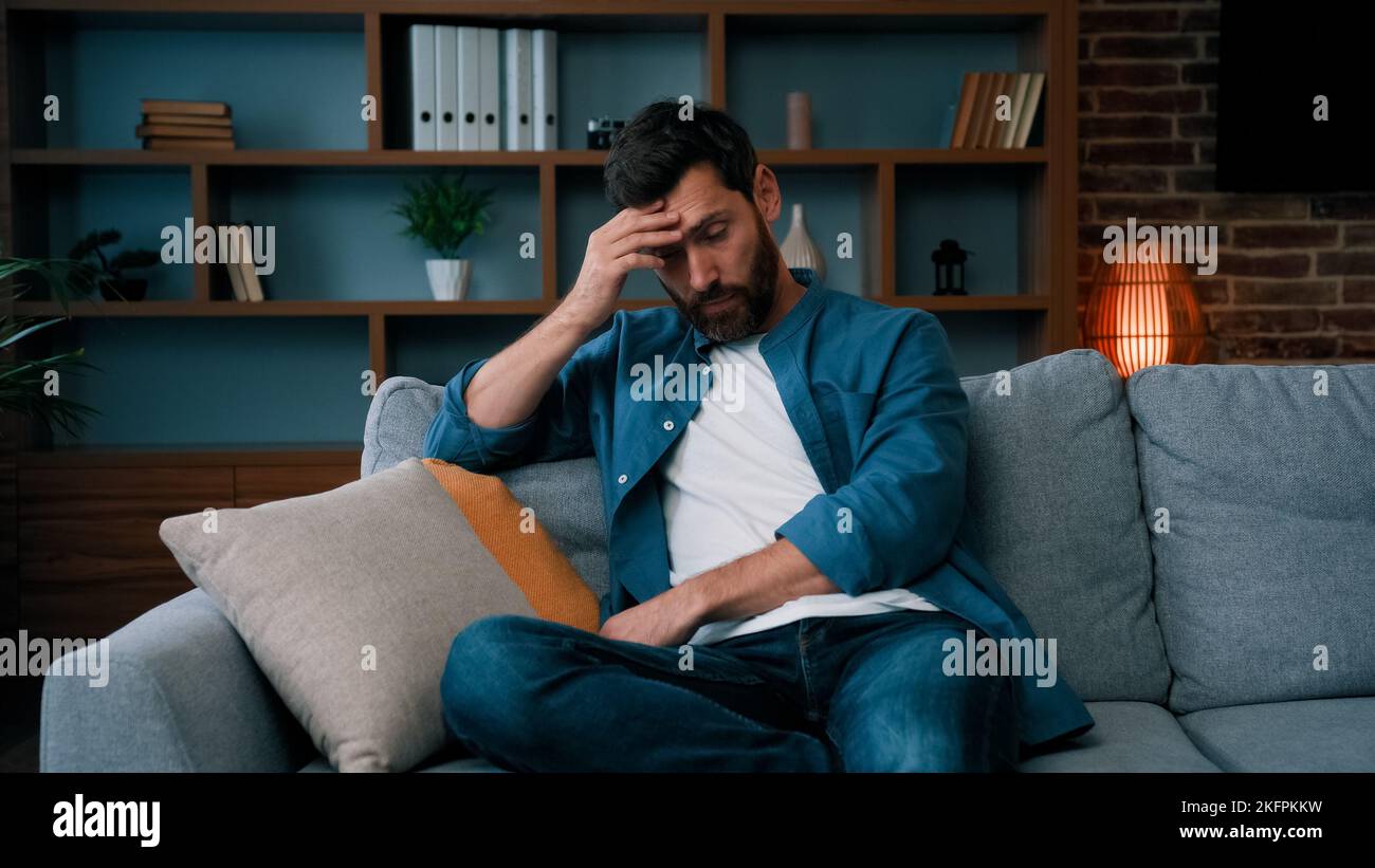 Stanco rovesciato padre caucasico uomo bearded sedersi sul divano frustrato circa duro giorno di lavoro a casa stressato singolo ragazzo preoccupato solitario maschio irritato Foto Stock