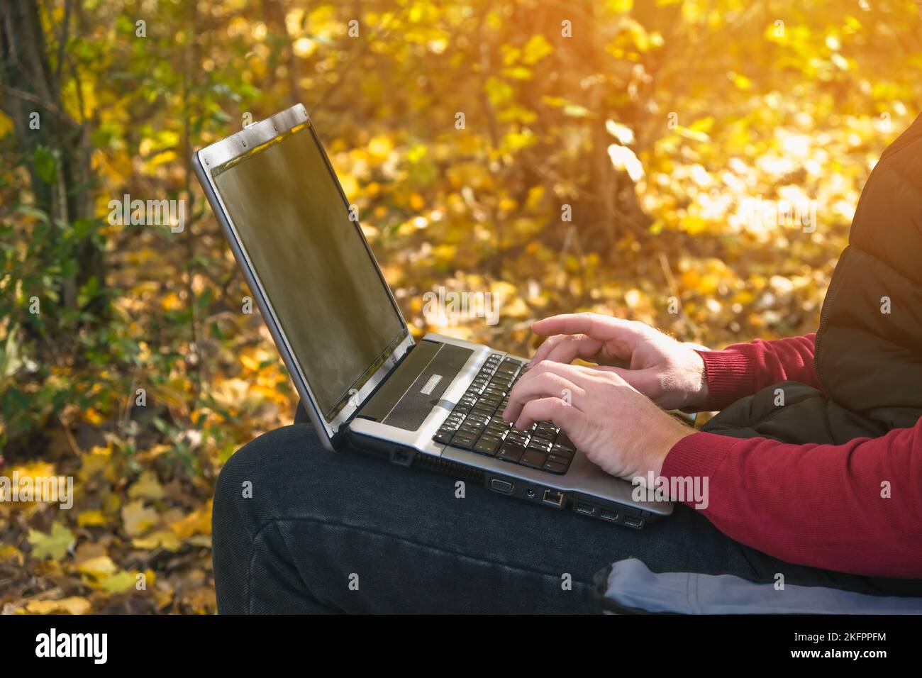 Un uomo freelance lavora a distanza in natura nella foresta autunnale. Vita di paese. Una pausa dalla civiltà. Van Lifevibes. Un uomo con un notebook. Apprendimento a distanza all'aria aperta tramite un computer portatile. Lavoro remoto. Foto Stock