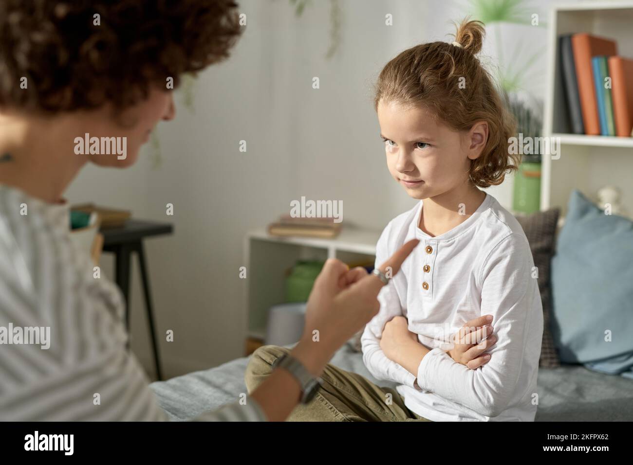 Naughty ragazzo seduto a letto con le braccia incrociate e ascoltando sua mamma parlare del suo cattivo comportamento Foto Stock