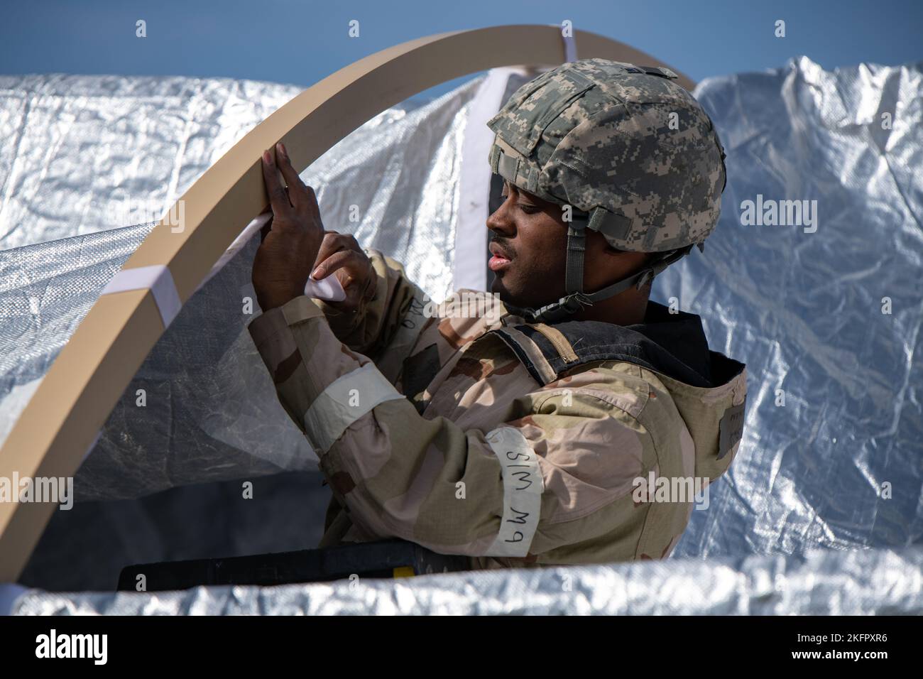 Senior Airmen Donovan Davis, 114th ingegnere civile Squadron ingegnere strutturale, costruisce una tenda da campo indossando dispositivi di protezione individuale (DPI) chimici, biologici, radiologici e nucleari (CBRN) durante un esercizio sul campo in diretta presso Joe Foss Field, South Dakota, 1 ottobre 2022. L’esercizio affina la competenza dell’unità nel rispondere a un attacco CBRN testandone la capacità di indossare rapidamente i dispositivi di protezione, valutare varie esposizioni chimiche, utilizzare le competenze TCCC (Tactical Combat Casualty Care) richieste per lo scenario e riprendere in sicurezza le operazioni di volo e addestramento. Foto Stock