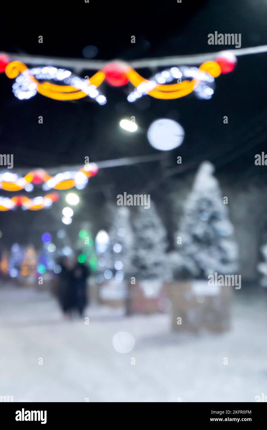 Sfondo sfocato astratto. Persone che camminano per strada di alberi di Natale decorati con illuminazione luminosa, luci incandescenti e ghirlande in città durante le pesanti nevicate nella notte d'inverno Foto Stock
