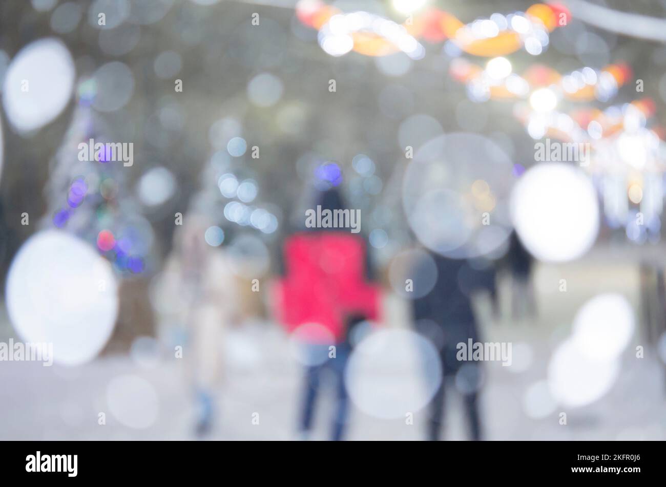 Sfondo sfocato astratto. Persone che camminano per strada di alberi di Natale decorati con illuminazione luminosa, luci incandescenti e ghirlande in città durante le pesanti nevicate nella notte d'inverno Foto Stock