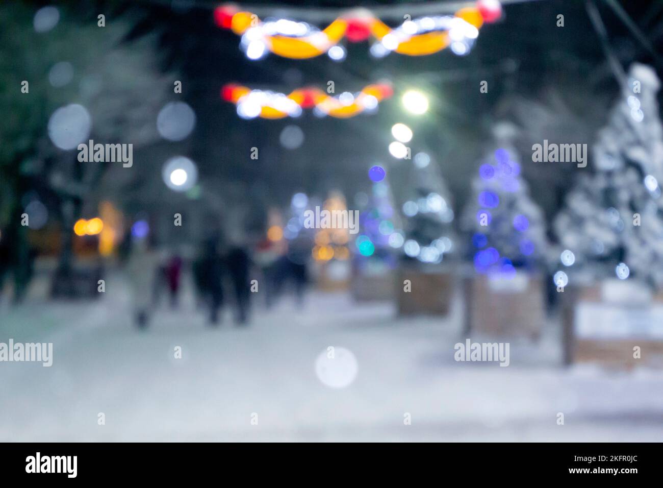Sfondo sfocato astratto. Persone che camminano per strada di alberi di Natale decorati con illuminazione luminosa, luci incandescenti e ghirlande in città durante le pesanti nevicate nella notte d'inverno Foto Stock