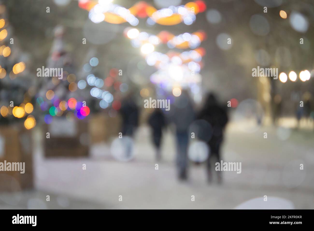 Sfondo sfocato astratto. Persone che camminano per strada di alberi di Natale decorati con illuminazione luminosa, luci incandescenti e ghirlande in città durante le pesanti nevicate nella notte d'inverno Foto Stock