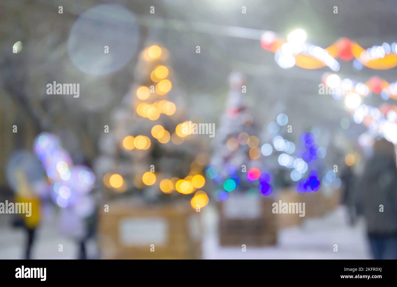 Sfondo sfocato astratto. Persone che camminano per strada di alberi di Natale decorati con illuminazione luminosa, luci incandescenti e ghirlande in città durante le pesanti nevicate nella notte d'inverno Foto Stock