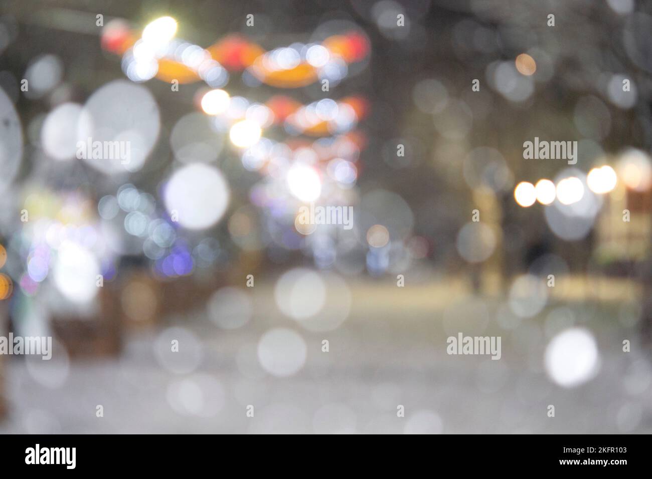 Sfondo sfocato astratto. Persone che camminano per strada di alberi di Natale decorati con illuminazione luminosa, luci incandescenti e ghirlande in città durante le pesanti nevicate nella notte d'inverno Foto Stock