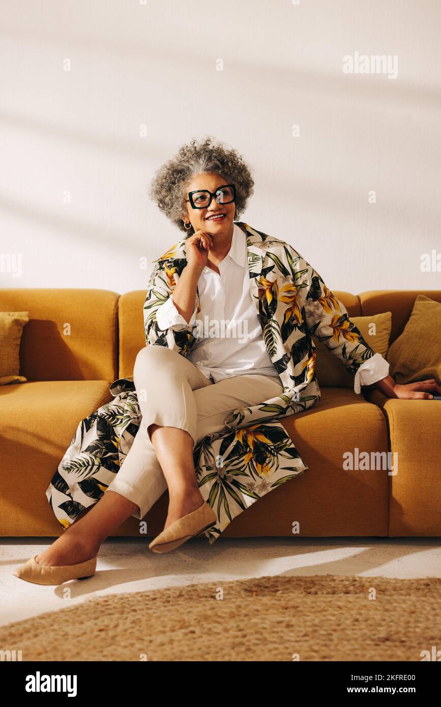 Donna d'affari penosa che guarda via con un sorriso mentre si siede su un divano in una lobby dell'ufficio. Donna d'affari premurosa che lavora in un college creativo Foto Stock