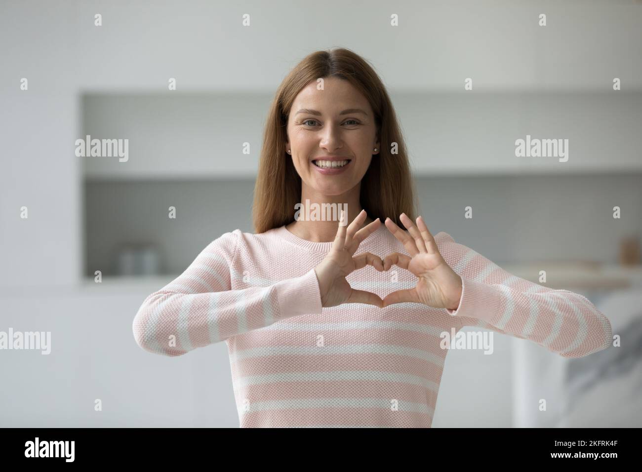 Giovane donna sorridente che mostra il segno del cuore con le dita Foto Stock
