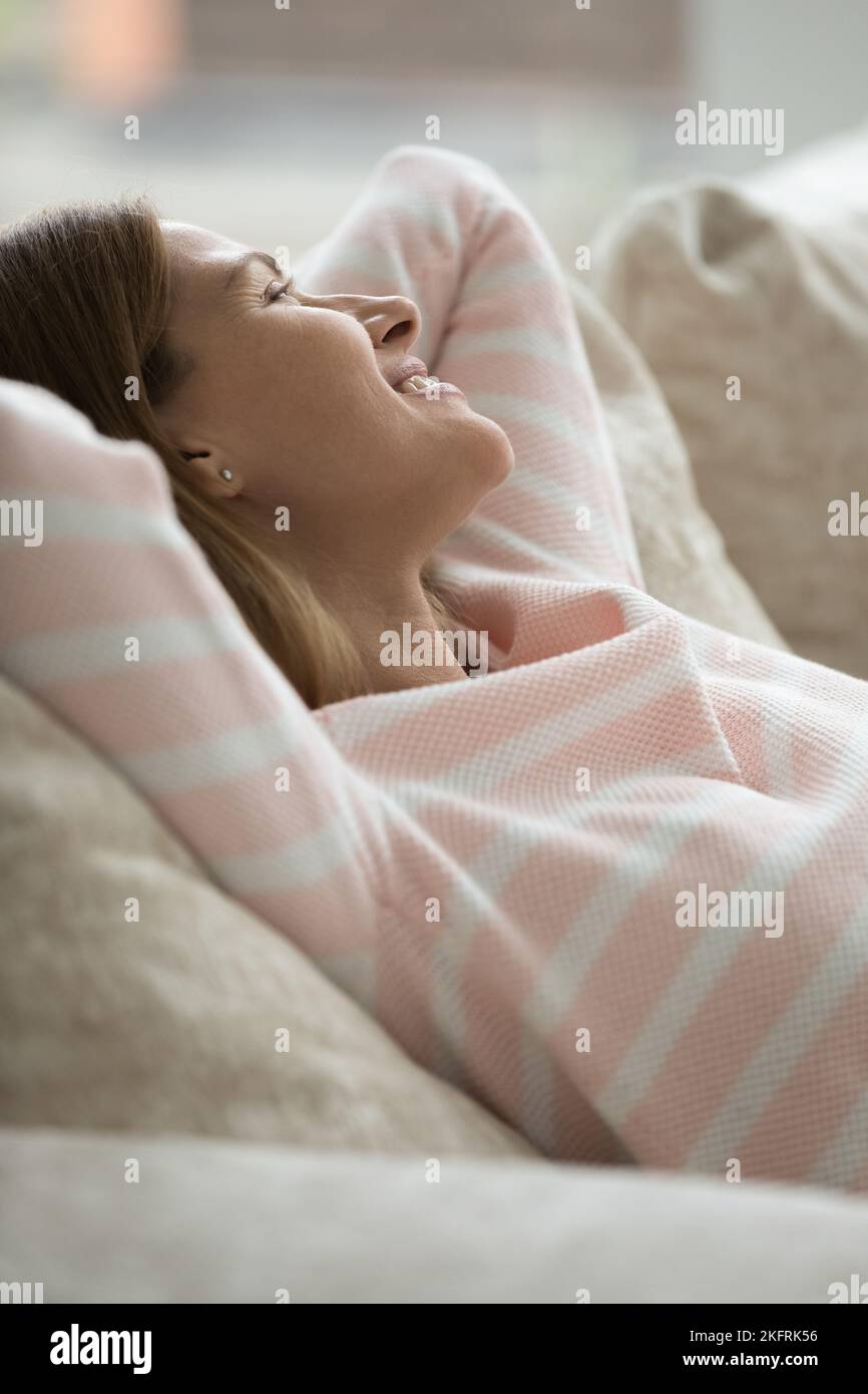 Colpo verticale felice donna che si rilassa sdraiata sui cuscini del divano Foto Stock
