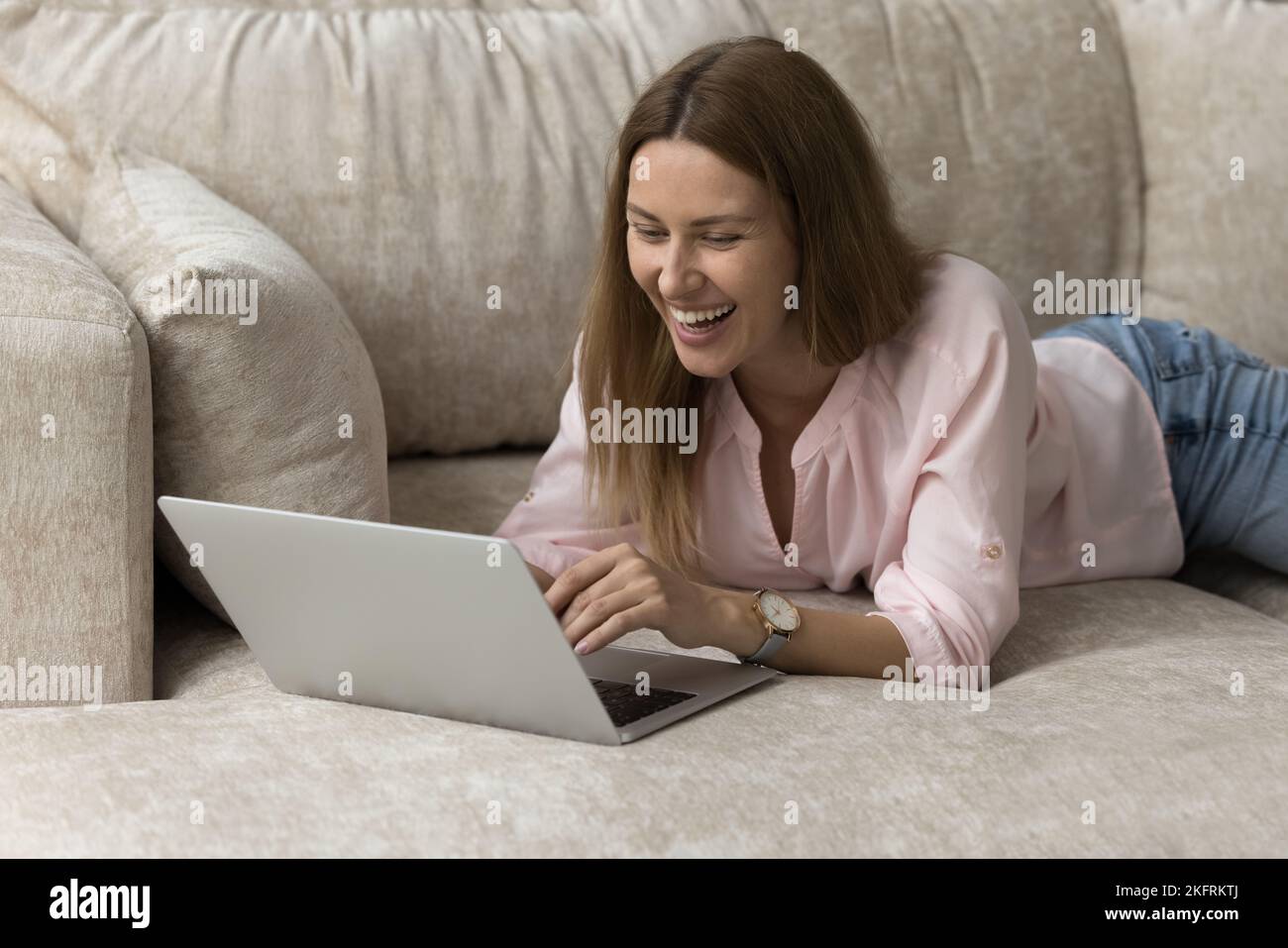 Donna sorridente Rilassati sul divano con il computer portatile, guarda un film online Foto Stock