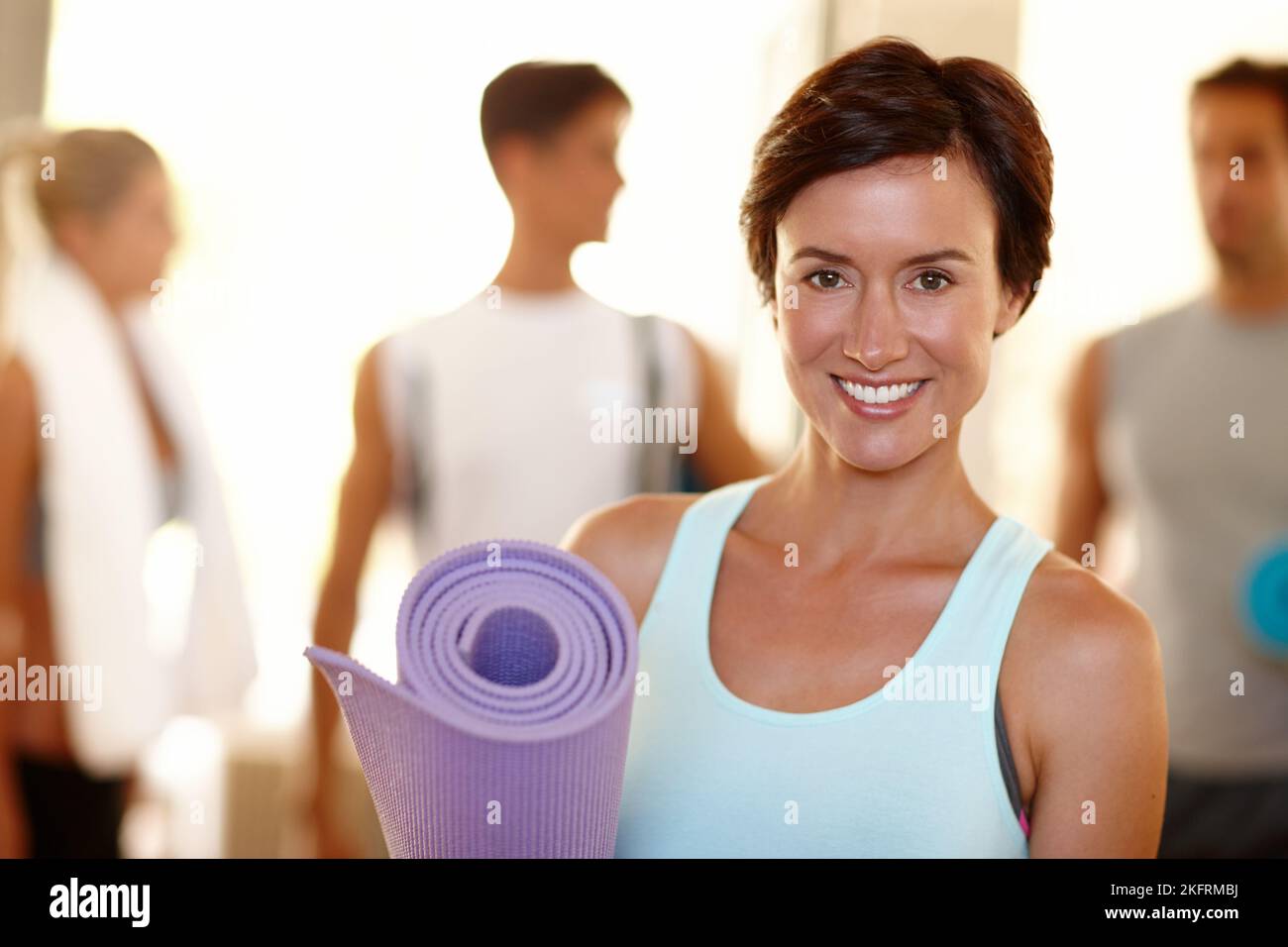 Sentirsi bene per il mio impegno di fitness. Ritratto di una bella donna con il suo materassino yoga e le persone sullo sfondo. Foto Stock