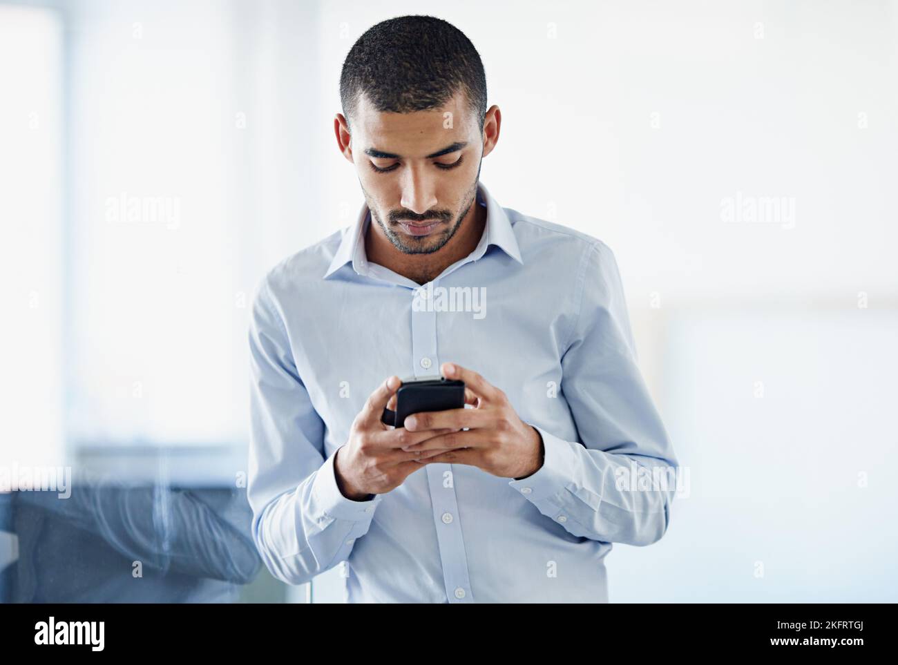 Mobilità aziendale. Un giovane uomo d'affari che invia un messaggio di testo mentre si trova in ufficio. Foto Stock