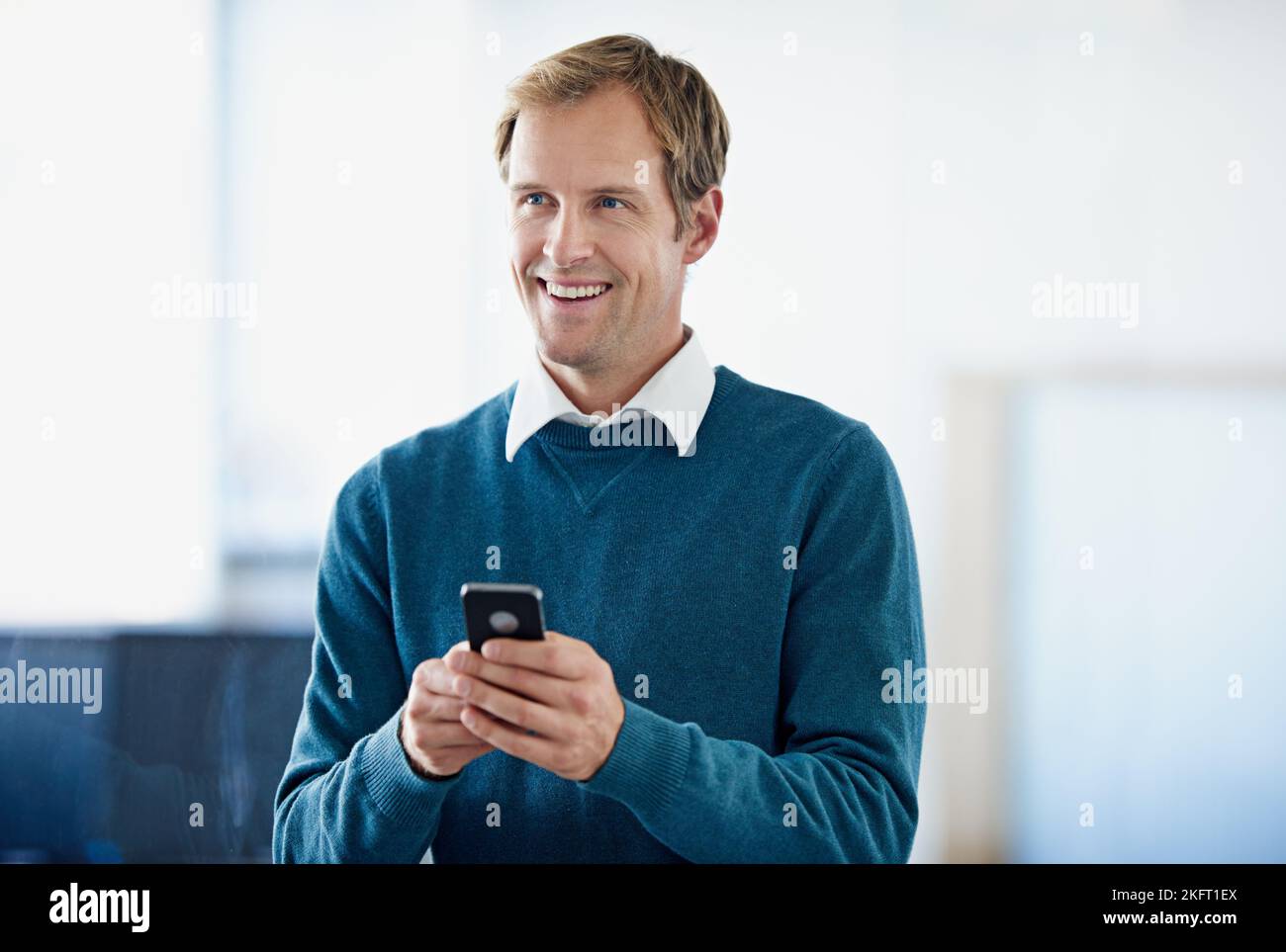 Un altro cliente soddisfatto. Un giovane uomo d'affari che invia un SMS mentre si trova in ufficio. Foto Stock