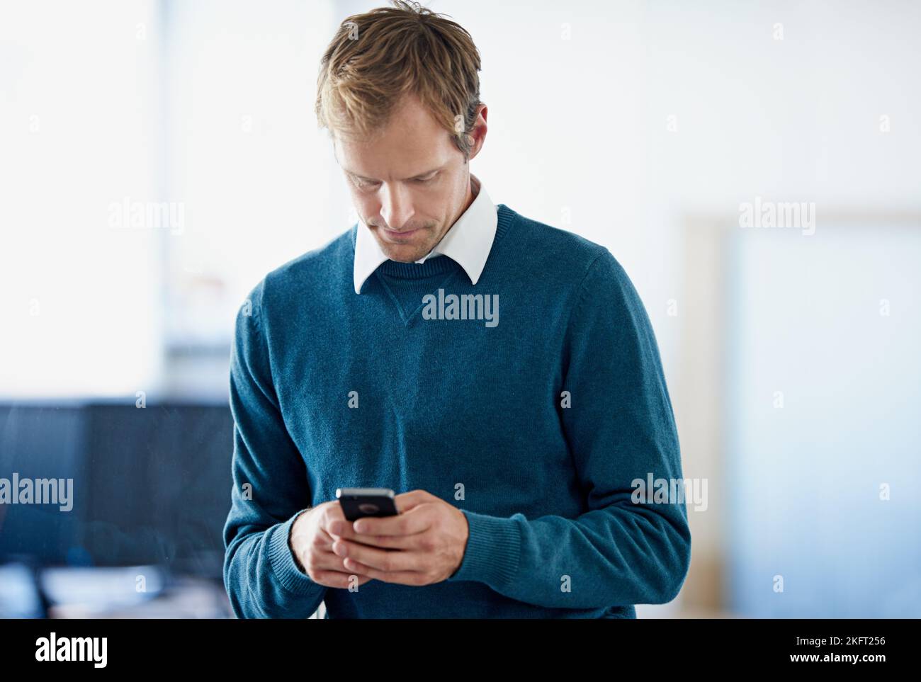 Comunicare con i clienti. Un giovane uomo d'affari che invia un messaggio di testo mentre si trova in un ufficio. Foto Stock