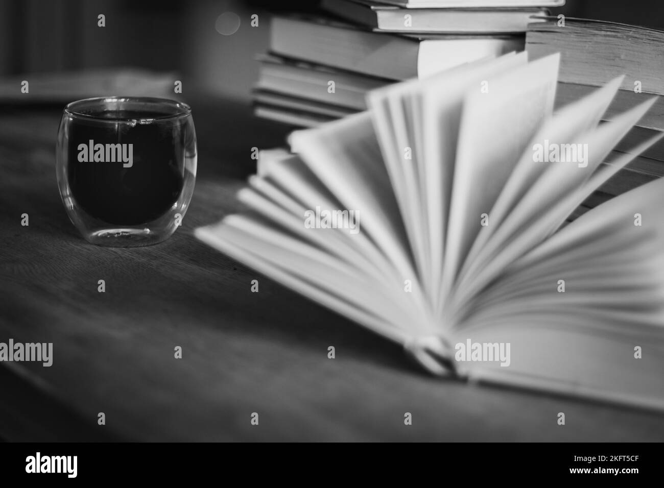 Pila di vecchi libri e tazza da caffè, in bianco e nero. Background letterario. Apri il libro e la pila di libri sul tavolo. Tempo caffè in biblioteca. Foto Stock