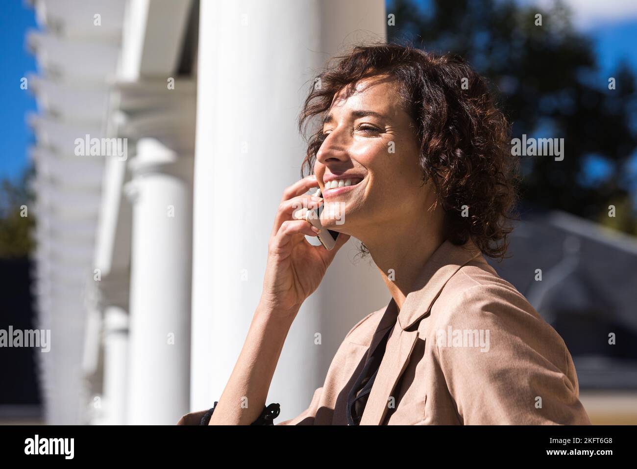 Vista laterale di una giovane donna d'affari con capelli ricci che parlano sul telefono cellulare il giorno di sole Foto Stock
