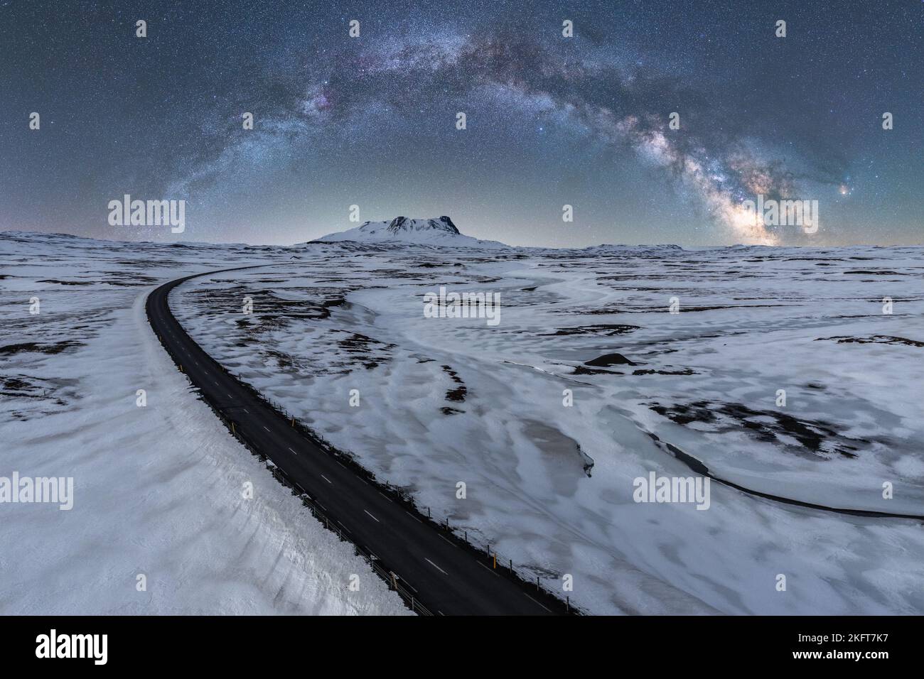 Vista da droni di una strada stretta e infinita che passa tra la terra ghiacciata sotto il cielo scintillante con la galassia Foto Stock