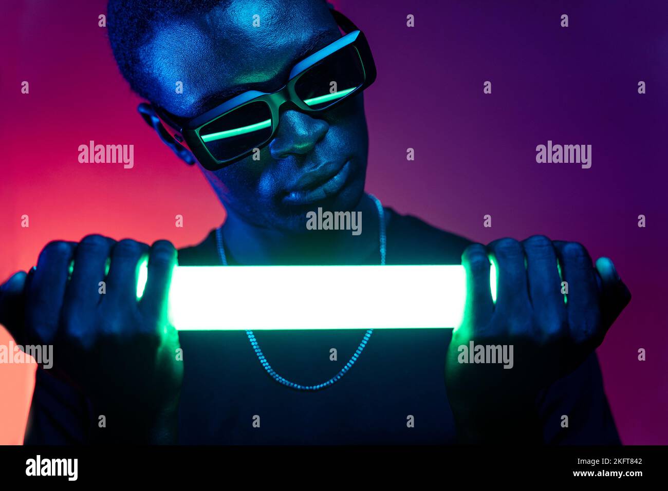Crop afro americano maschio con catena sul collo e occhiali da sole che riflettono luce brillante di neon luce Foto Stock