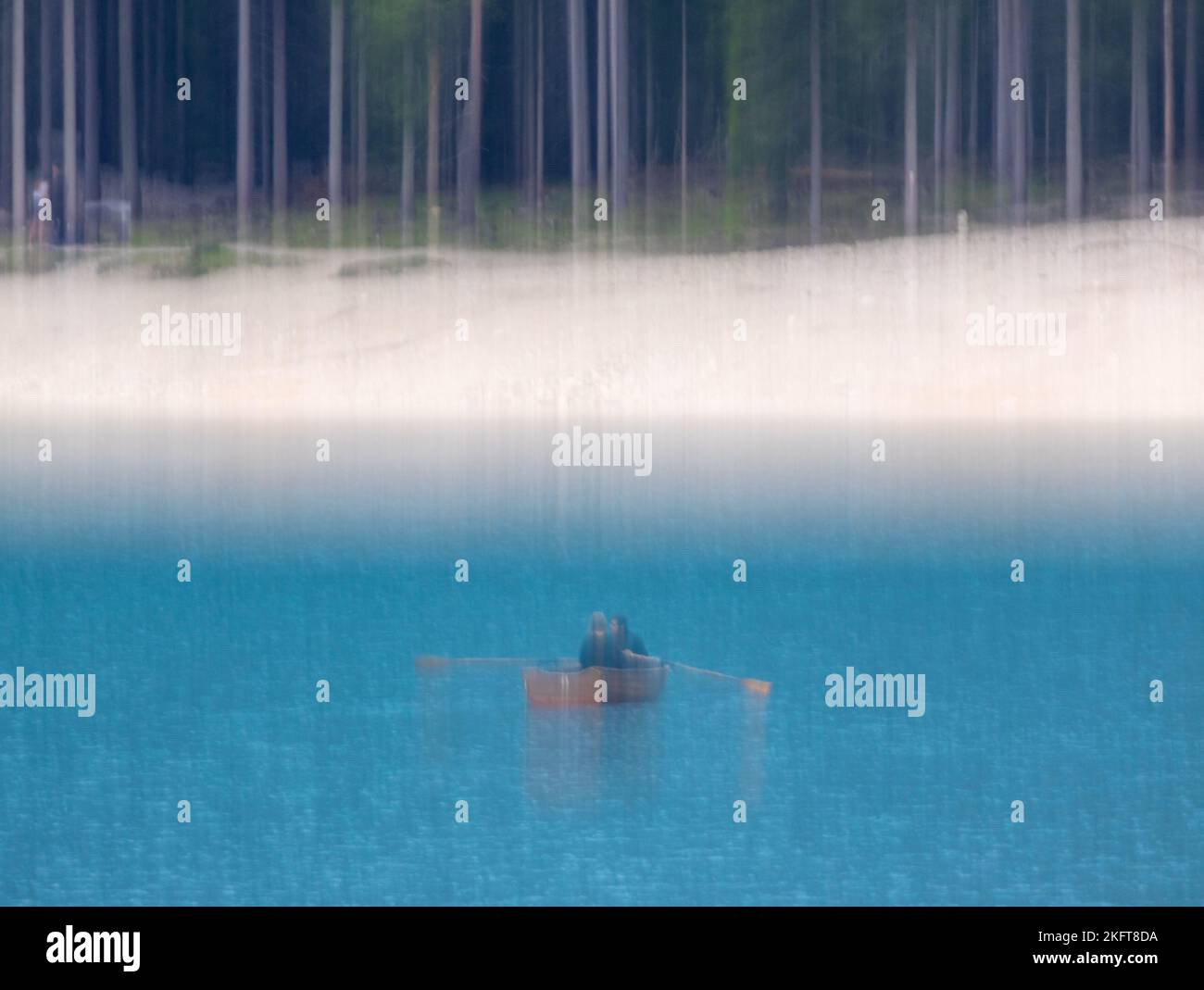 Immagine sfocata in movimento verticale di persone che galleggiano sulla barca a remi con pagaie in acqua blu ondeggiante vicino a boschi verdi Foto Stock