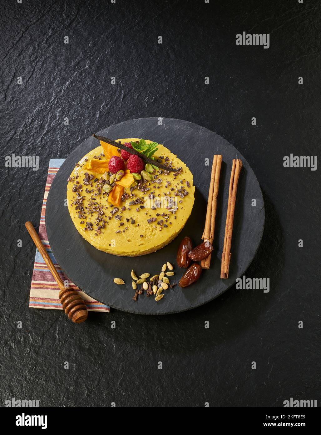 Dall'alto di gustosa torta gialla decorata con lamponi e baccello di vaniglia vicino al miele cucchiaia su tovagliolo Foto Stock