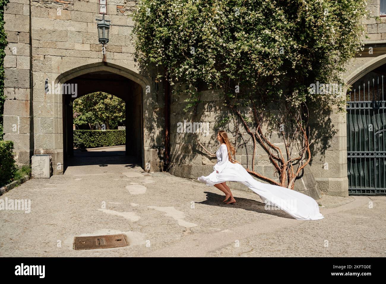 una bella donna in un vestito bianco cammina attraverso un bel palazzo in una giornata di sole Foto Stock