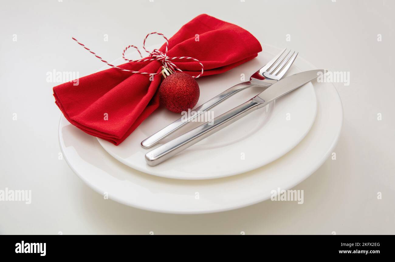 Cena di Capodanno a Natale. Impostazione del tavolo delle festività. Posate argentate e tovagliolo rosso su piatto bianco, vista ravvicinata. Foto Stock