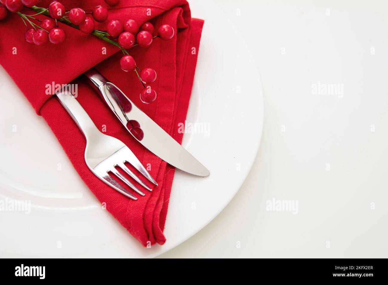 Impostazione del tavolo delle festività. Posate argentate e tovagliolo rosso su piatto bianco, vista ravvicinata. Cena di Capodanno a Natale Foto Stock