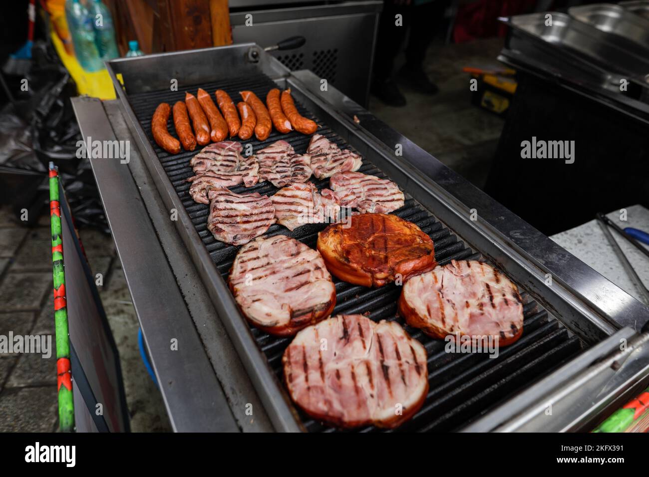 Profondità di campo bassa (fuoco selettivo) dettagli con salsicce di maiale e bistecche che cucinano su una griglia barbecue, in un mercato agricolo europeo, a Bucarest Foto Stock
