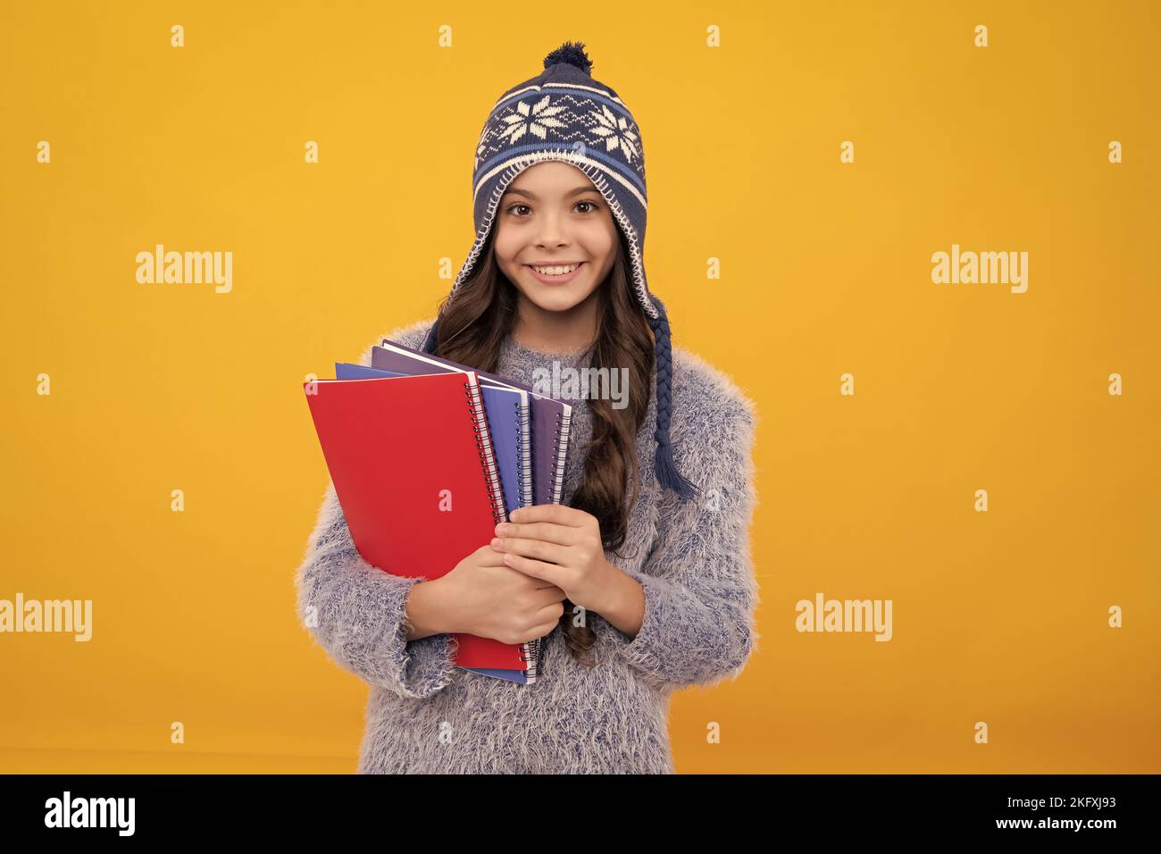 Vacanze scolastiche invernali. Ritorno a scuola. Studentessa adolescente con cappello caldo e maglione su sfondo giallo isolato studio. Scuola invernale. Foto Stock
