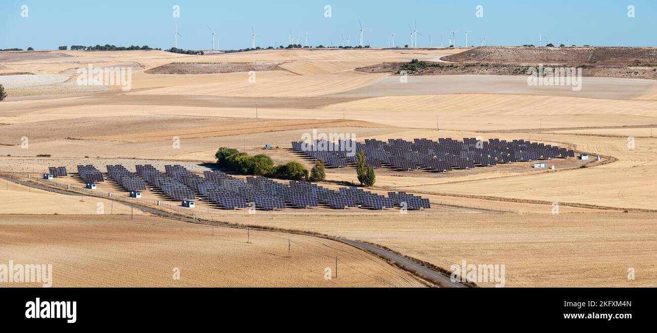 Vista aerea di una centrale fotovoltaica nella campagna al di fuori di Valladolid in Spagna, con alcuni mulini a vento sullo sfondo. Foto Stock