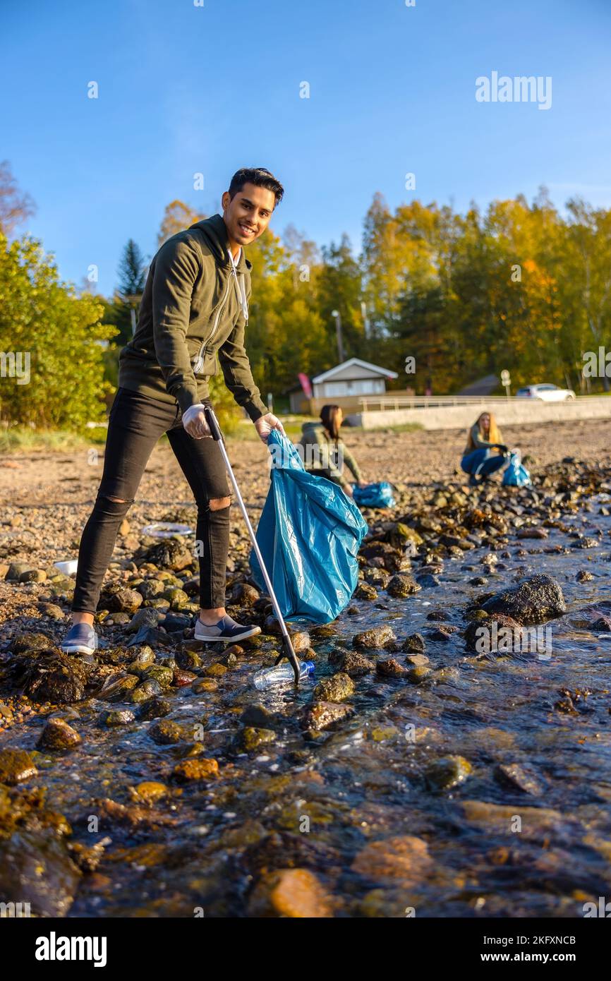 Giovane uomo sorridente che pulisce l'oceano con volontari nelle giornate di sole Foto Stock