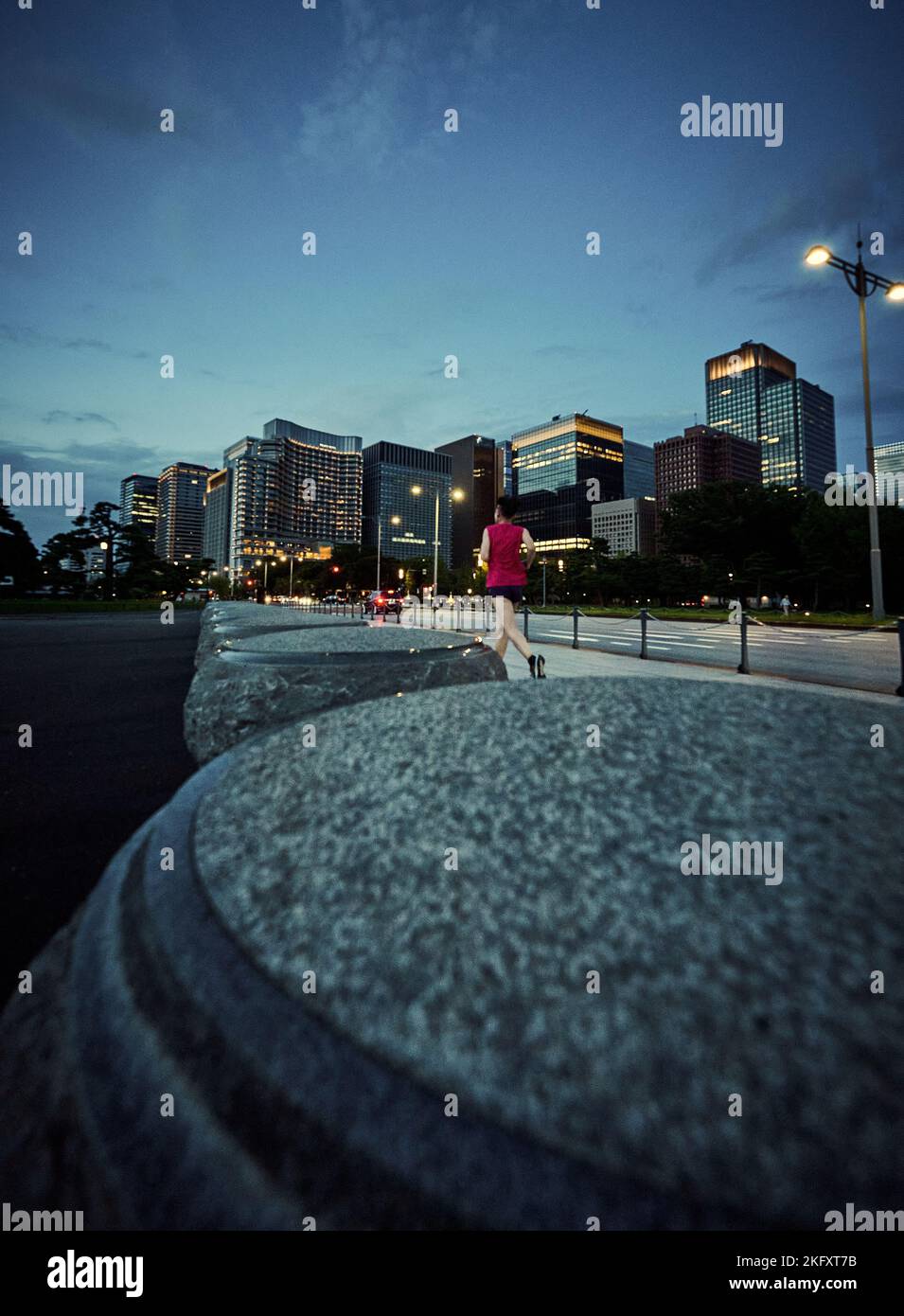 Uno scatto verticale di una persona che corre per strada la sera e le architetture sullo sfondo Foto Stock