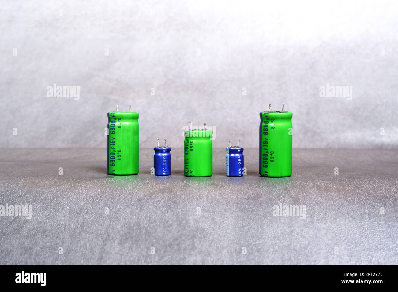 Condensatori elettrolitici di varie dimensioni sono disposti in fila sul pavimento in cemento Foto Stock